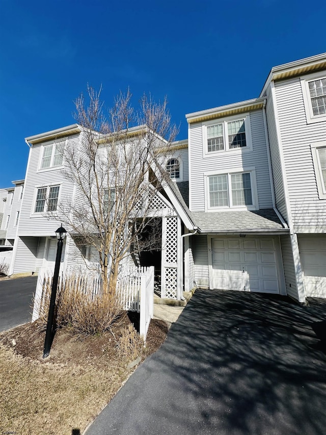 multi unit property with driveway, a shingled roof, and an attached garage