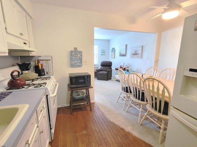 kitchen featuring white appliances, white cabinetry, under cabinet range hood, and hardwood / wood-style floors