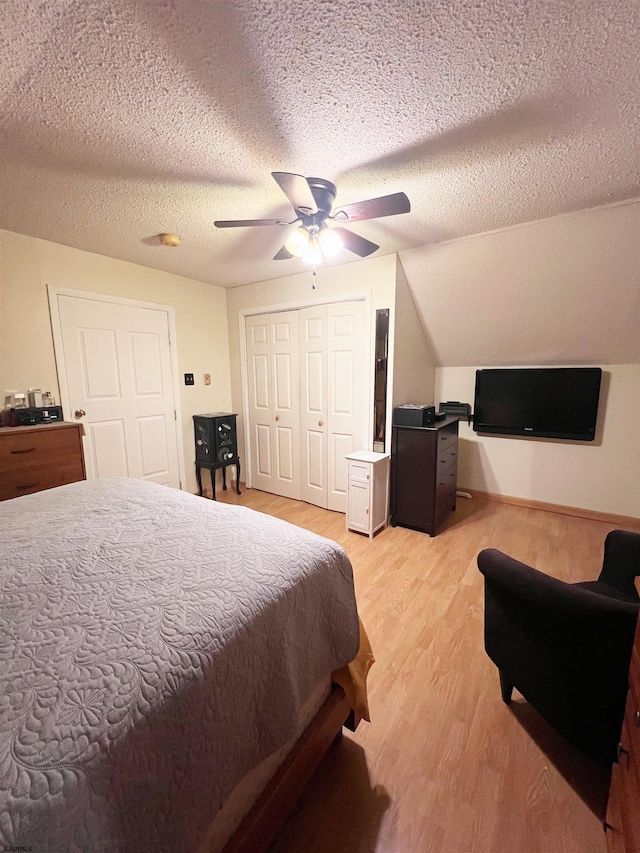 bedroom with a ceiling fan, lofted ceiling, a textured ceiling, light wood-style floors, and a closet
