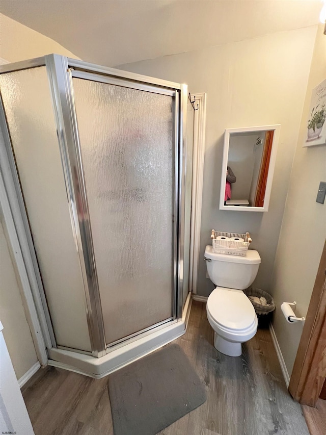 bathroom featuring toilet, a shower stall, baseboards, and wood finished floors