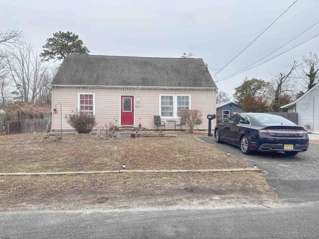 view of front facade with entry steps, a shingled roof, fence, and aphalt driveway