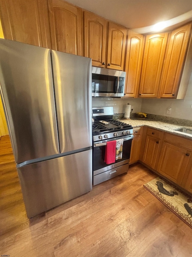 kitchen featuring stainless steel appliances, light wood finished floors, brown cabinetry, and a sink