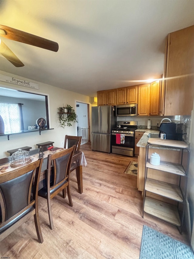 kitchen with light wood finished floors, appliances with stainless steel finishes, brown cabinets, light countertops, and a sink