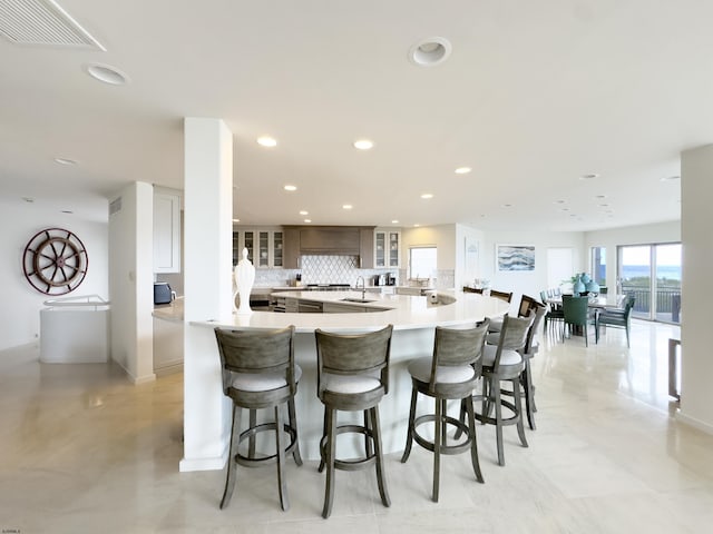 kitchen featuring visible vents, glass insert cabinets, light countertops, a kitchen bar, and backsplash