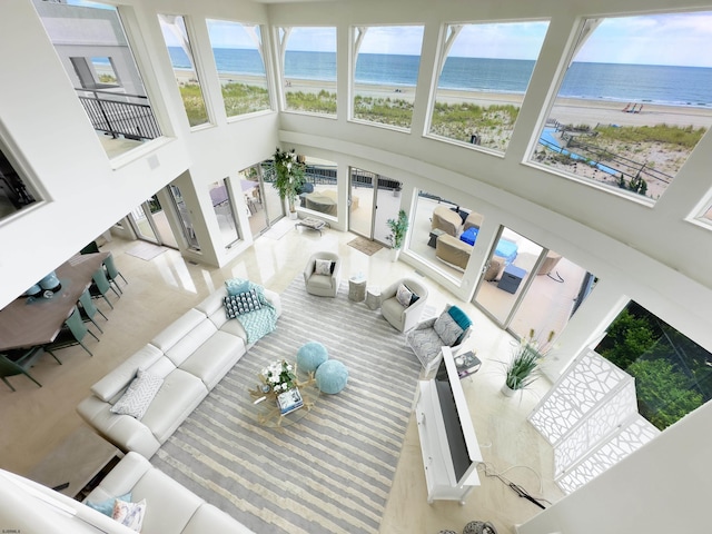 sunken living room featuring a view of the beach, a water view, and a high ceiling