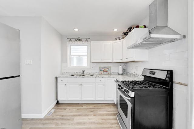 kitchen with light stone counters, freestanding refrigerator, white cabinets, gas range, and extractor fan