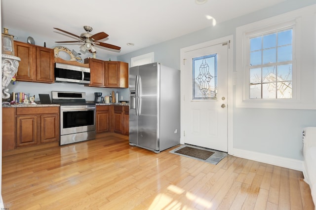 kitchen with brown cabinets, light wood finished floors, stainless steel appliances, and a ceiling fan