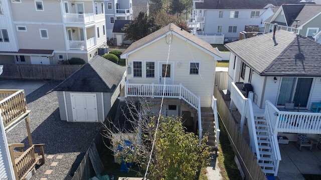 back of property with an outbuilding, a storage unit, stairway, central AC, and fence