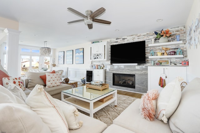 living room with a fireplace, decorative columns, light wood-style flooring, a ceiling fan, and beverage cooler