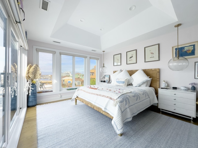 bedroom with wood finished floors, a raised ceiling, and visible vents