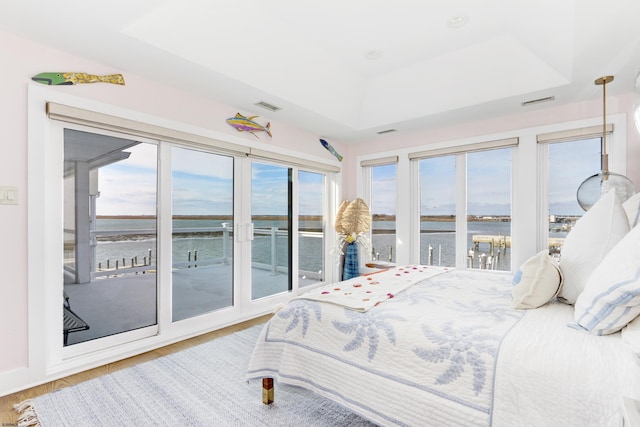 bedroom with a tray ceiling, a water view, visible vents, wood finished floors, and access to outside