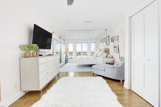 bedroom with light wood-type flooring, ceiling fan, visible vents, and baseboards