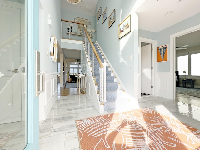 foyer with marble finish floor, stairs, a decorative wall, and wainscoting