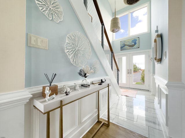 entryway with wainscoting, a towering ceiling, stairs, french doors, and a decorative wall