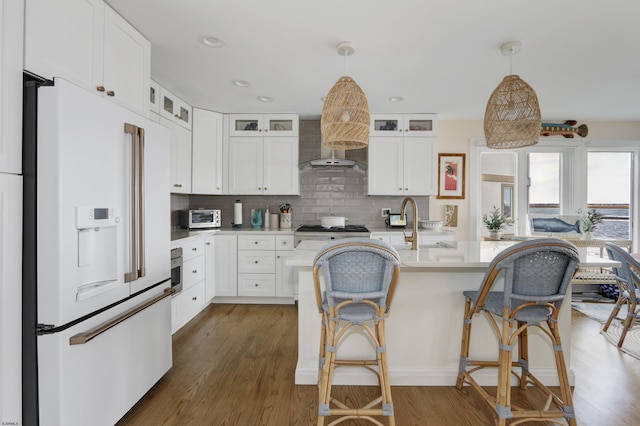 kitchen with light countertops, high end white fridge, glass insert cabinets, white cabinetry, and wall chimney exhaust hood