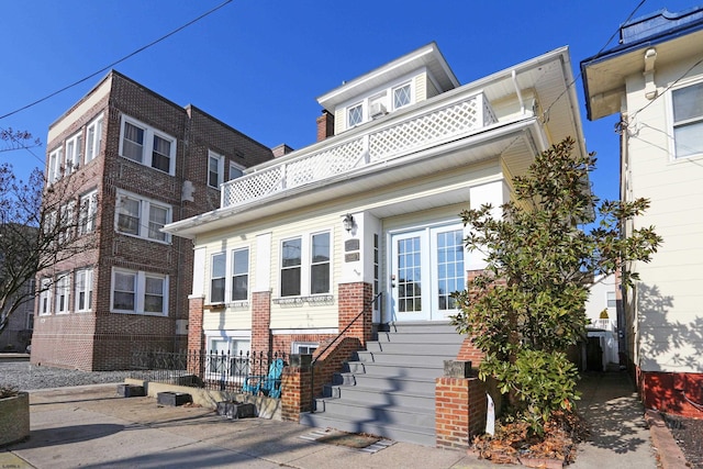 view of front of home featuring entry steps, french doors, brick siding, and a balcony