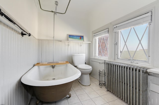 bathroom with a freestanding bath, toilet, radiator heating unit, wainscoting, and tile patterned floors