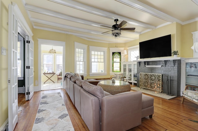 living area featuring ornamental molding, beamed ceiling, light wood-style flooring, and a healthy amount of sunlight