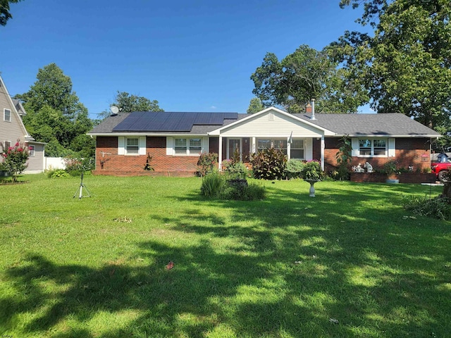 single story home with roof mounted solar panels, brick siding, and a front lawn