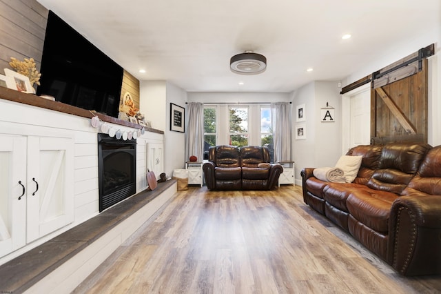 living room featuring recessed lighting, wood finished floors, a fireplace with raised hearth, and a barn door