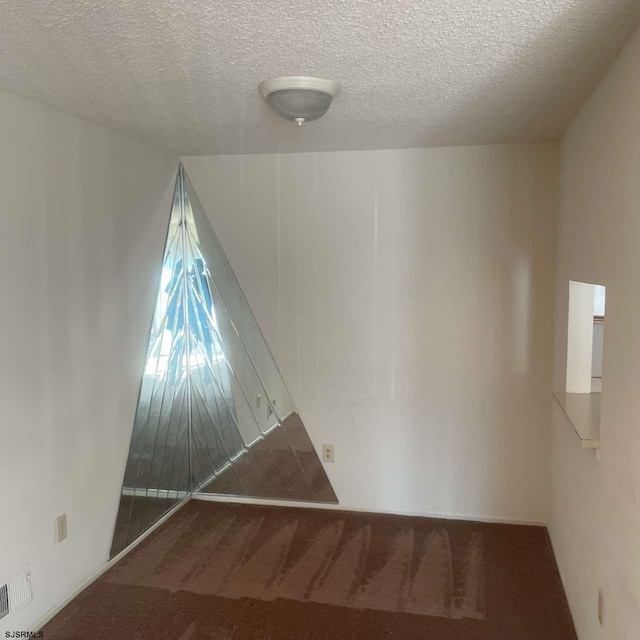 empty room featuring a textured ceiling, carpet flooring, and visible vents