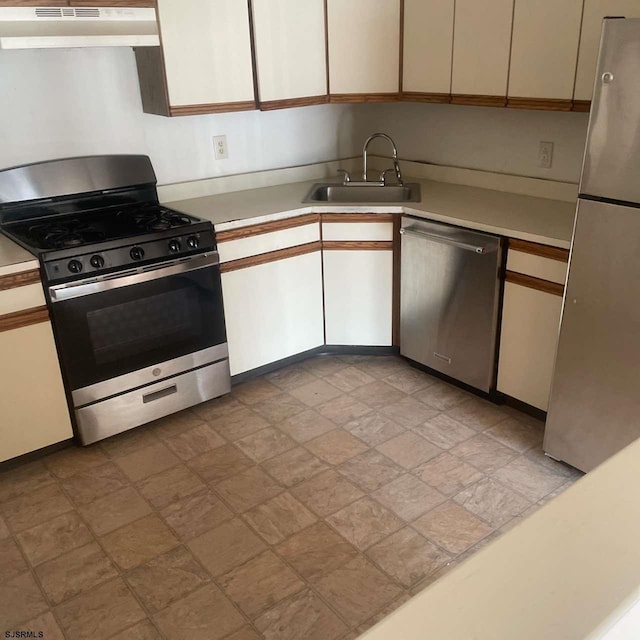 kitchen with white cabinets, stainless steel appliances, light countertops, under cabinet range hood, and a sink