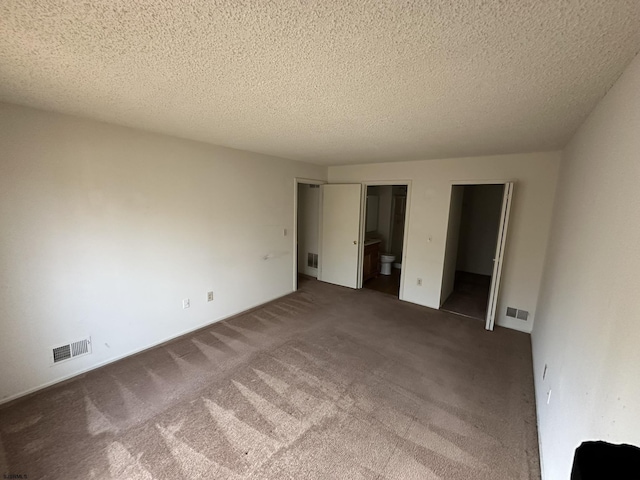 unfurnished bedroom with visible vents, dark carpet, and connected bathroom