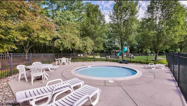 pool with a patio area, playground community, and fence