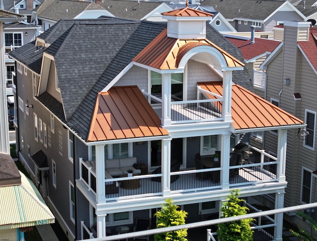 back of house featuring metal roof, a shingled roof, a standing seam roof, and a balcony