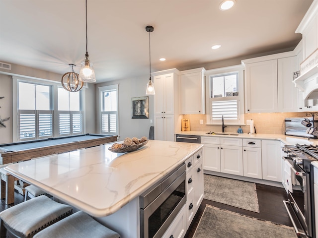 kitchen with hanging light fixtures, light stone countertops, stainless steel appliances, a kitchen bar, and white cabinetry