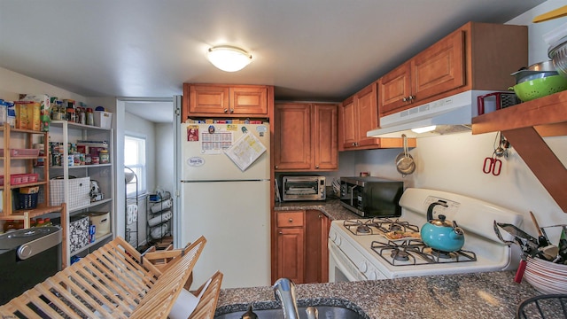 kitchen featuring a toaster, under cabinet range hood, white appliances, a sink, and brown cabinetry