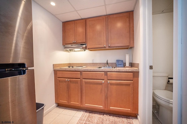 kitchen featuring light tile patterned floors, light countertops, freestanding refrigerator, a sink, and under cabinet range hood