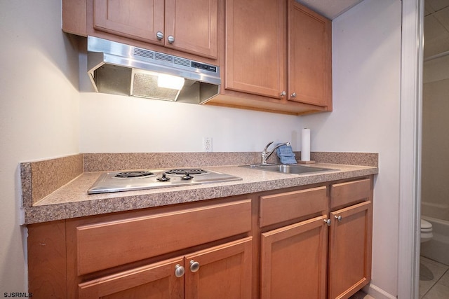 kitchen featuring brown cabinets, stovetop, a sink, and under cabinet range hood