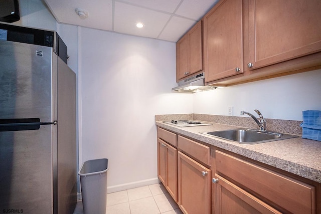 kitchen featuring light tile patterned floors, under cabinet range hood, a sink, freestanding refrigerator, and white electric stovetop