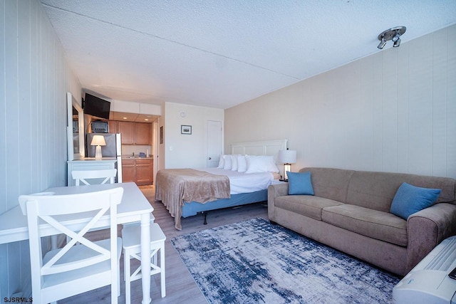 bedroom with freestanding refrigerator, a textured ceiling, and wood finished floors