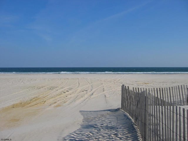 property view of water featuring a view of the beach and fence