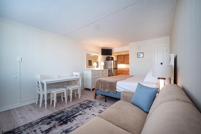 bedroom featuring freestanding refrigerator, a textured ceiling, and wood finished floors