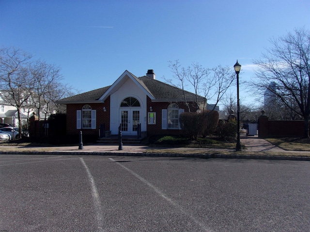 view of front of property featuring french doors, brick siding, roof with shingles, a chimney, and uncovered parking