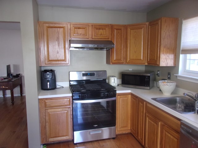 kitchen featuring under cabinet range hood, wood finished floors, a sink, light countertops, and appliances with stainless steel finishes