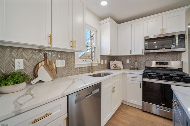 kitchen with light stone counters, stainless steel appliances, a sink, white cabinetry, and light wood-style floors