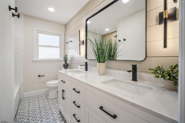 full bathroom with baseboards, a sink, toilet, and double vanity