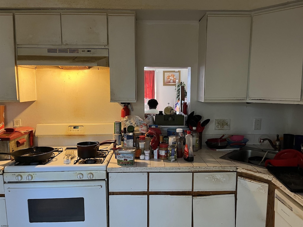 kitchen featuring white appliances, white cabinetry, under cabinet range hood, and tile countertops