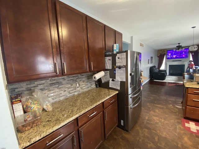 kitchen featuring light stone counters, a fireplace, decorative backsplash, open floor plan, and stainless steel fridge with ice dispenser