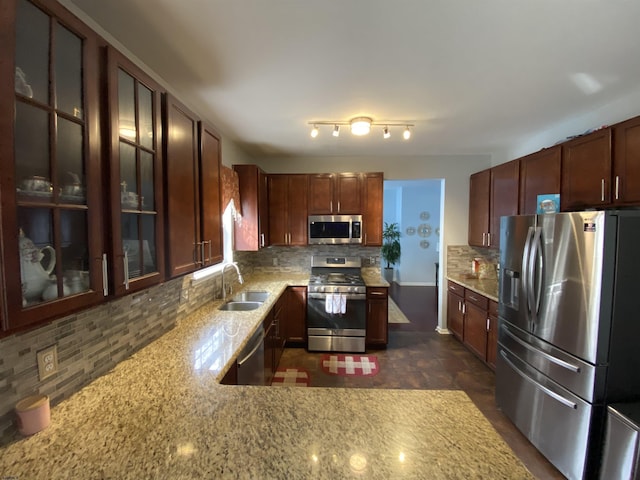 kitchen with light stone counters, stainless steel appliances, backsplash, glass insert cabinets, and a sink