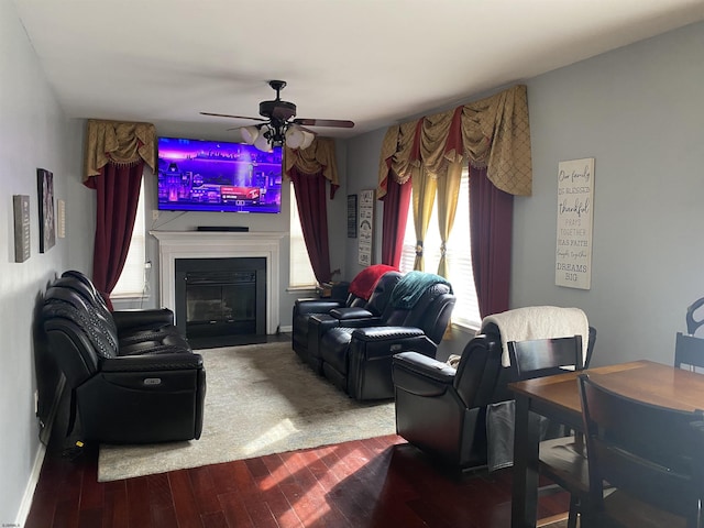 living area featuring ceiling fan, a glass covered fireplace, wood finished floors, and baseboards