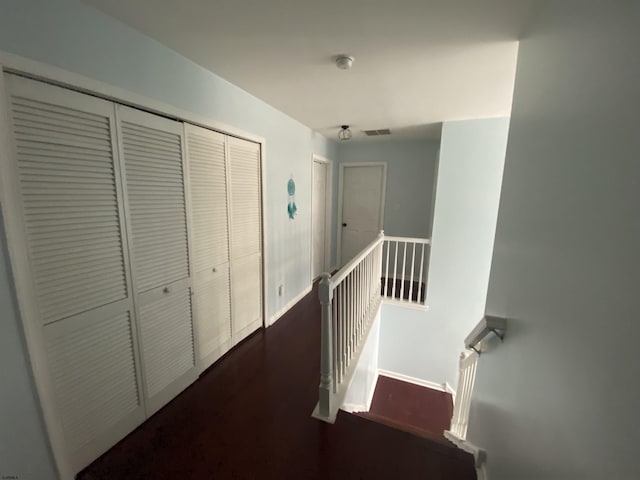 hallway with baseboards, visible vents, dark wood-type flooring, and an upstairs landing