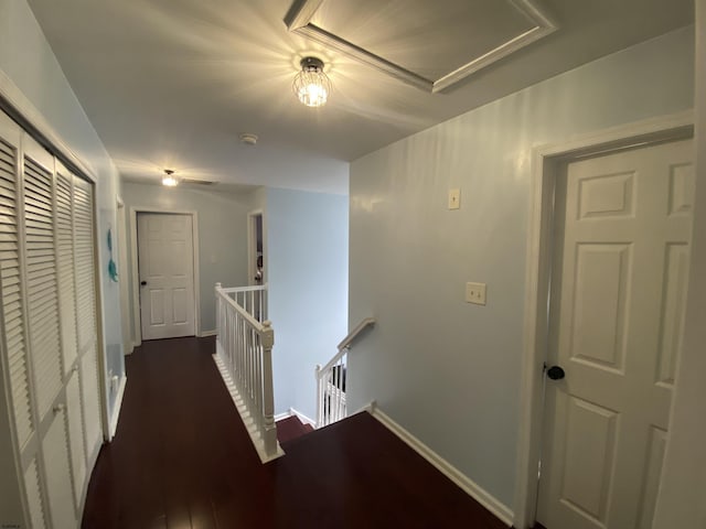 hall featuring dark wood-style floors, baseboards, and an upstairs landing