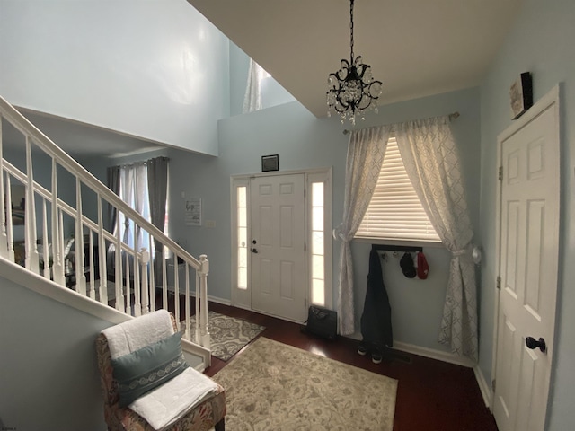 foyer with a notable chandelier, a towering ceiling, stairway, dark wood-type flooring, and baseboards