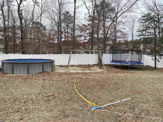 view of yard with a fenced in pool, a fenced backyard, and a trampoline