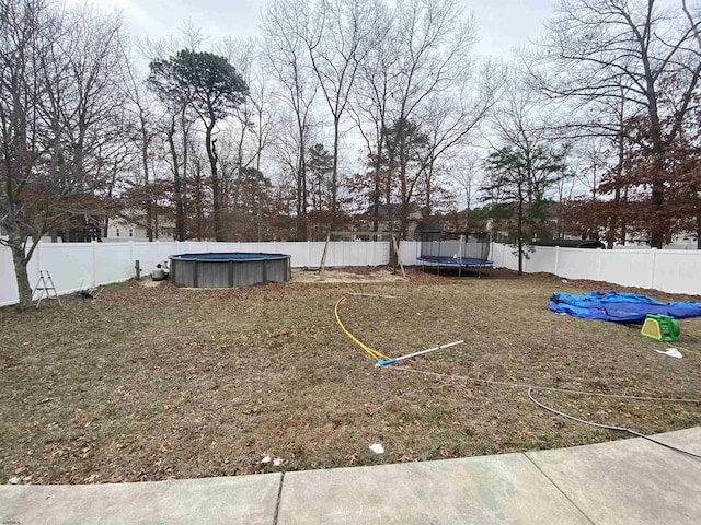 view of yard featuring a trampoline, a fenced backyard, and a fenced in pool